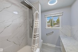 Bathtub with a multi-function shower panel, marble-look tile surround, and a coordinating marble-look vanity countertop - 