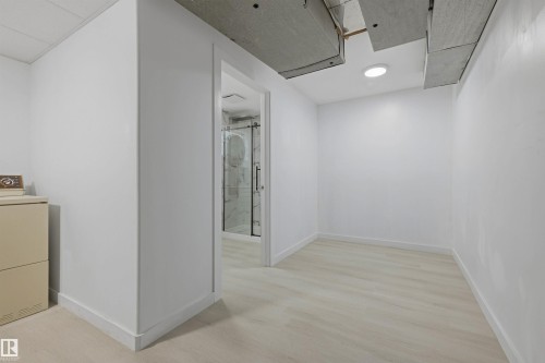 Wood-finish flooring with white baseboards, recessed lighting, and a doorway to an additional room featuring a glass-enclosed shower - 13024 Sherbrooke Avenue Nw, Edmonton, AB 