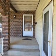 Brick exterior with a concrete porch and steps, featuring a full-light storm door and a wall-mounted light fixture - 