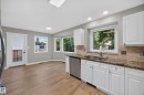 Kitchen featuring white cabinetry, granite countertops, tile backsplash, stainless steel dishwasher, and wood-finish flooring - 3640 31 Street Nw, Edmonton, AB 