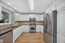 White cabinetry with paneled doors, stainless steel appliances, wood-finish flooring, recessed lighting, and a window - 