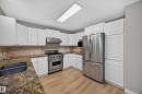White cabinetry, stainless steel appliances, wood-finish flooring, stone-finish countertops, and a tile backsplash - 3640 31 Street Nw, Edmonton, AB 
