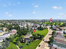 Aerial view of a residential area featuring numerous homes, expansive green spaces, a public park with play equipment, and mature trees - 