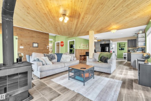 Open-concept living area featuring a wood-finish plank ceiling, wood-finish flooring, and a free-standing wood-burning stove - 5103 50 Street, Cold Lake, AB - Indoor Photo Showing Living Room