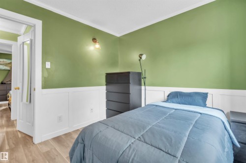 Room featuring two-tone walls with white wainscoting and green paint, wood-finish flooring, white crown molding, and a white interior door with a gold-tone knob - 5103 50 Street, Cold Lake, AB - Indoor Photo Showing Bedroom
