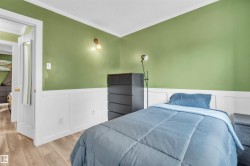 Room featuring two-tone walls with white wainscoting and green paint, wood-finish flooring, white crown molding, and a white interior door with a gold-tone knob - 