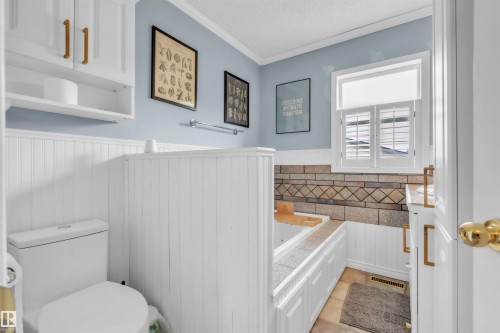 Bathroom featuring a built-in tub with tile surround, white beadboard wainscoting, and a window with white louvered shutters - 5103 50 Street, Cold Lake, AB - Indoor Photo Showing Bathroom