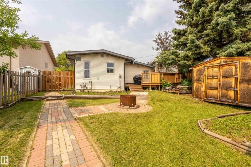 Expansive backyard featuring a brick paver pathway, a built-in fire pit with a surrounding paver patio, mature trees, and a wooden storage shed - 5103 50 Street, Cold Lake, AB - Outdoor With Deck Patio Veranda