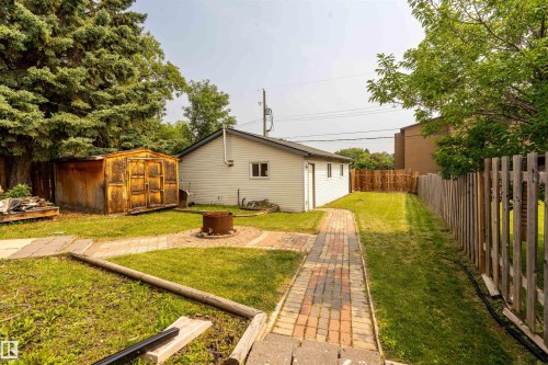 Expansive backyard featuring a brick paver pathway, mature trees, a wooden fence, and a detached building with siding - 5103 50 Street, Cold Lake, AB - Outdoor