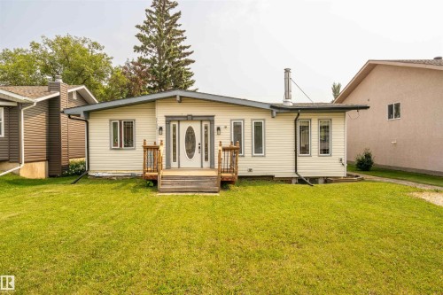 Cream-colored siding exterior featuring a white oval glass paneled front door, flanked by two exterior wall sconces and a wooden deck entry - 5103 50 Street, Cold Lake, AB - Outdoor