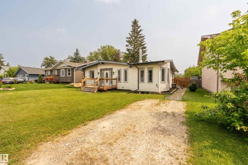 White siding exterior with a gravel driveway, front wooden deck, and mature landscaping - 5103 50 Street, Cold Lake, AB - Outdoor