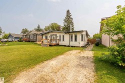 White siding exterior with a gravel driveway, front wooden deck, and mature landscaping - 