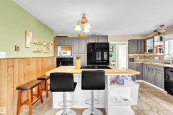 Kitchen featuring a central island with a wood countertop and built-in cooktop, gray cabinetry with gold-tone hardware, a tiled backsplash, and stone-look floor tiles - 