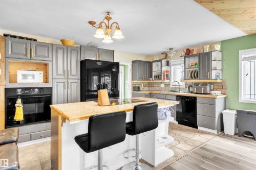 Kitchen featuring gray cabinetry, light-toned countertops, a center island with bar seating, integrated black appliances, and a mix of tile and wood-finish flooring - 5103 50 Street, Cold Lake, AB - Indoor