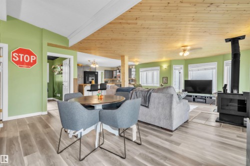 Open-concept living area featuring wood-finish flooring, a wood plank ceiling, light green walls, a black freestanding stove, and multiple windows - 5103 50 Street, Cold Lake, AB - Indoor