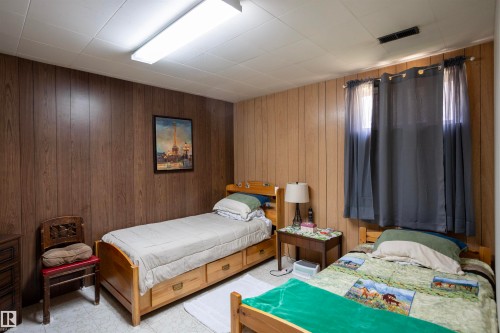 Room featuring wood-look paneling walls, a white acoustic tile ceiling, and a large fluorescent ceiling light fixture - 10428 68 Avenue Nw, Edmonton, AB 