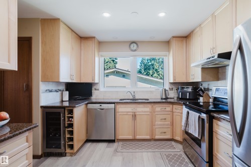 U-shaped kitchen with light wood cabinetry, stone countertops, stainless steel appliances, a built-in wine refrigerator, and wood-finish flooring - 10924 35A Avenue Nw, Edmonton, AB 