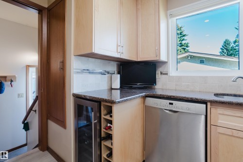 Granite-finish countertops, light wood-finish cabinetry, stainless steel dishwasher, tile backsplash, and built-in wine storage - 10924 35A Avenue Nw, Edmonton, AB 