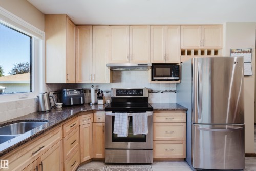 Light wood-finish cabinetry, stainless steel appliances, dark granite-style countertops, and a tiled backsplash - 10924 35A Avenue Nw, Edmonton, AB 