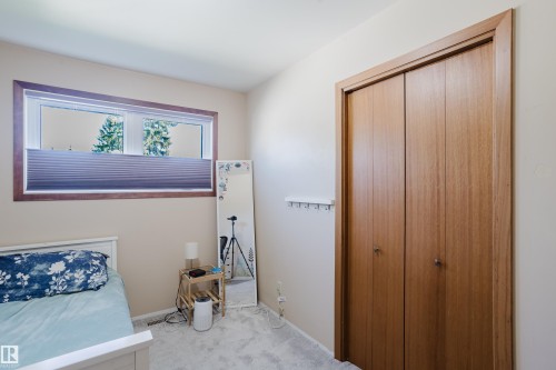 Light-colored wall paint with a horizontal window featuring a cellular shade, wood-toned window trim, and a wood-toned bi-fold closet door - 10924 35A Avenue Nw, Edmonton, AB 