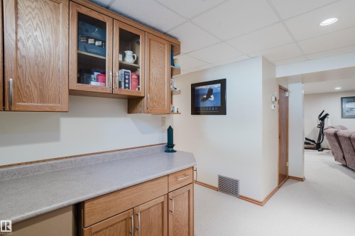 Wood-finish cabinetry with glass-front uppers and a light-toned countertop - 10924 35A Avenue Nw, Edmonton, AB 