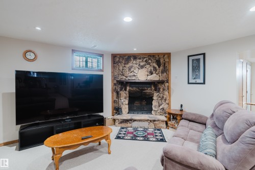 Stone fireplace with hearth, recessed lighting, wood-trimmed window, and neutral carpeting - 10924 35A Avenue Nw, Edmonton, AB 