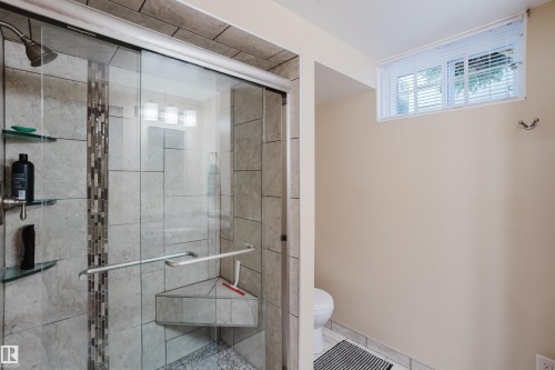 Glass-enclosed shower with a tiled surround, built-in corner bench, and mosaic tile accent - 10924 35A Avenue Nw, Edmonton, AB 