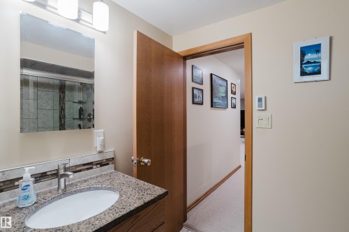 Bathroom featuring a granite-finish vanity, undermount sink, and tile backsplash - 10924 35A Avenue Nw, Edmonton, AB 