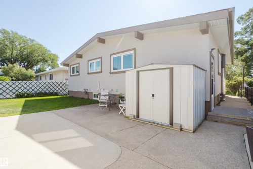 Expansive concrete patio with a detached storage shed, lush green lawn, and a decorative lattice fence - 10924 35A Avenue Nw, Edmonton, AB 