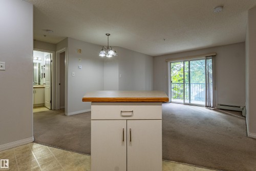 Open-concept living area with carpet flooring, a ceiling-mounted light fixture, and a sliding glass door leading to a balcony - #316 11325 83 St Nw, Edmonton, AB 
