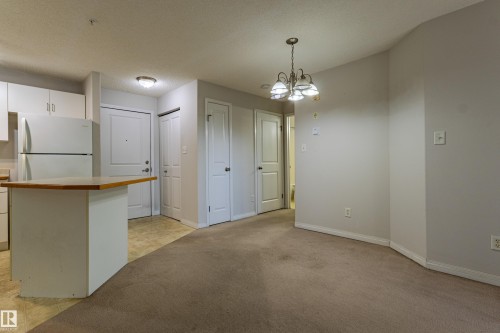Kitchen area with white cabinetry, a refrigerator, and a breakfast bar - #316 11325 83 St Nw, Edmonton, AB 