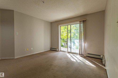 Sliding glass door leading to a balcony with metal railing, carpeted flooring, and neutral wall paint - #316 11325 83 St Nw, Edmonton, AB 
