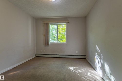 Window with vertical blinds, carpet flooring, baseboard heating, ceiling-mounted light fixture, and textured ceiling - #316 11325 83 St Nw, Edmonton, AB 