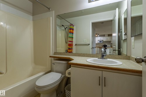 Bathroom featuring a tub/shower combination, a vanity with an integrated sink, a large wall mirror, and a toilet - #316 11325 83 St Nw, Edmonton, AB 