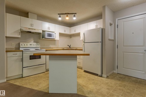 Kitchen featuring white cabinetry, light wood-finish countertops, and a full suite of white appliances - #316 11325 83 St Nw, Edmonton, AB 