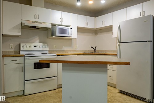 Kitchen featuring white cabinetry, wood-finish countertops, and an integrated kitchen island - #316 11325 83 St Nw, Edmonton, AB 