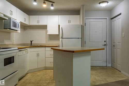 Kitchen featuring white cabinetry, built-in appliances, a corner sink, wood-finish countertops, and an integrated island - #316 11325 83 St Nw, Edmonton, AB 