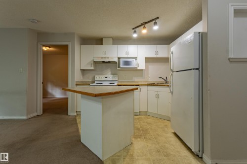 Kitchen featuring white cabinetry, track lighting, and a white appliance package including a range, microwave, and refrigerator - #316 11325 83 St Nw, Edmonton, AB 