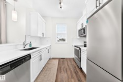 Galley kitchen featuring white cabinetry, stainless steel appliances, wood-finish flooring, white subway tile backsplash, and a window for natural light - 