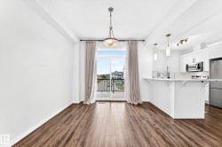 Open-concept living space featuring wood-finish flooring, a sliding glass door with balcony access, and a kitchen with white cabinetry and stainless steel appliances - 
