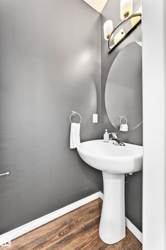 Pedestal sink with chrome faucet, oval mirror, and wood-finish flooring - 20008 19 Avenue Nw, Edmonton, AB 