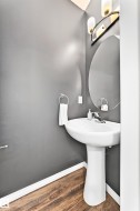 Pedestal sink with chrome faucet, oval mirror, and wood-finish flooring - 
