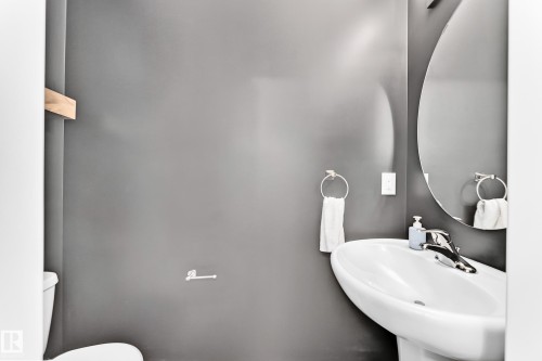 Pedestal sink with chrome faucet, oval wall mirror, and neutral wall color - 20008 19 Avenue Nw, Edmonton, AB 