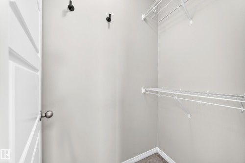 White wire shelving, dark gray carpet, matte black wall hooks, and a paneled interior door with a brushed nickel knob - 20008 19 Avenue Nw, Edmonton, AB 