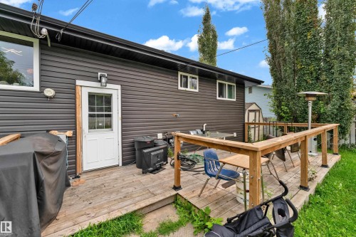 Exterior featuring dark horizontal siding, white trim windows, a white paneled door with glass, and a wooden deck with railings - 14216 58 Street Nw, Edmonton, AB 