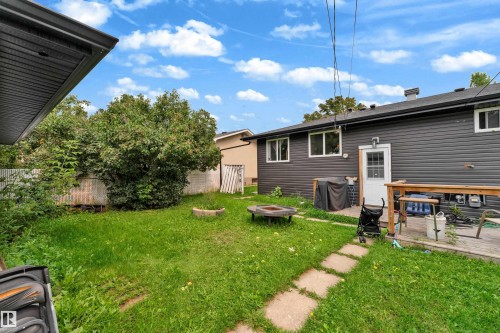 Expansive backyard featuring a manicured lawn, established trees, a concrete paver pathway, and a wood deck - 14216 58 Street Nw, Edmonton, AB 