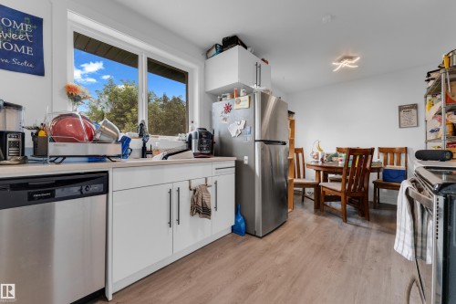 Stainless steel dishwasher, light wood-finish flooring, white cabinetry with dark hardware, recessed lighting, and a large window - 14216 58 Street Nw, Edmonton, AB 