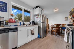 Stainless steel dishwasher, light wood-finish flooring, white cabinetry with dark hardware, recessed lighting, and a large window - 