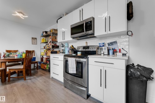 White cabinetry, stainless steel appliances, white subway tile backsplash, wood-finish flooring, and a contemporary ceiling fixture - 14216 58 Street Nw, Edmonton, AB 