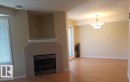 Tiled fireplace with a mantel, wood-finish flooring, and a multi-light chandelier - #9 2505 42 St Nw, Edmonton, AB 
